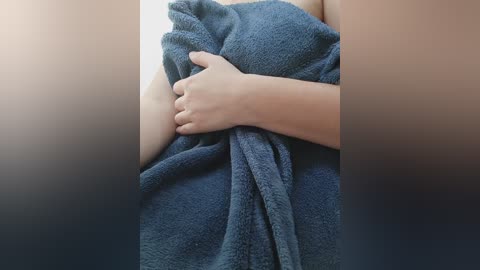 Video of a person's arm wrapped in a dark blue, plush towel, with a blurred background suggesting a bathroom setting. The image focuses on the texture and warmth of the towel.