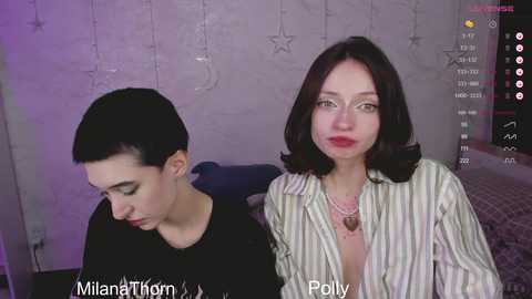 Media: Video of two women in a dimly lit room, with one having short dark hair and the other with shoulder-length dark hair, wearing a striped shirt.