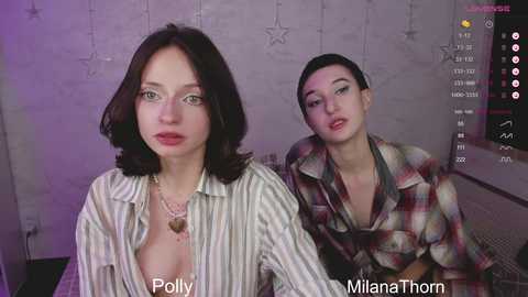 Media: Video of two women, one with a pale complexion, dark hair, and a striped shirt, and the other with a fair complexion, short dark hair, and a plaid shirt, set against a dimly lit, star-patterned wall.
