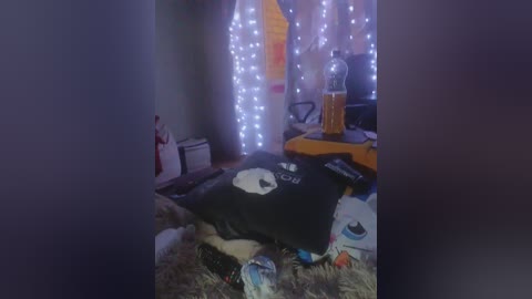 A video of a messy bedroom with a black pillow featuring a white panda character, a glass of orange juice, and fairy lights on the wall.