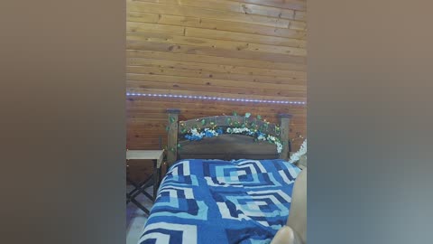 A video of a cozy bedroom with a wooden headboard, blue and white patterned bedspread, and a wooden wall adorned with string lights. The room features a rustic, cabin-like aesthetic.