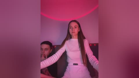 Media: Video of a woman in white, long-sleeved jumpsuit, holding a man's head, with a red light background.