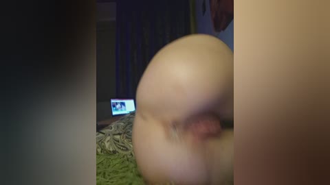 A dimly lit video of a naked person with a large, round buttocks, viewed from behind, positioned on a green rug. A television screen shows an image in the background.