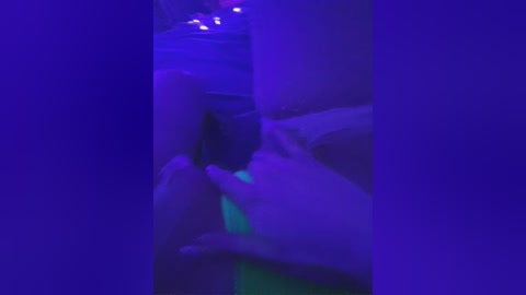 A blurry video of a person's hand holding a small, glowing object against a dark, purple background. The hand's fingers are spread, and the object emits a soft, blue light.
