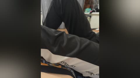 A video shows a person kneeling on a gym mat, wearing black sweatpants with a white sports logo. The background reveals a blurry indoor setting with gym equipment.
