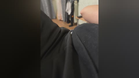 Video of a person wearing black clothing, with a blurred background showing a closet filled with clothes. The focus is on the person's arm and part of their body.