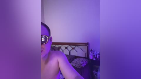Video of a nude person with a VR headset on, partially visible, in a dimly lit bedroom with purple lighting.