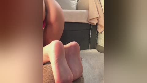 Video of a person's bare feet on a beige carpet, with a focus on the soles. The background shows a beige sofa with a light pink blanket. The setting appears to be a living room.