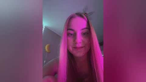Media: A video of a young, fair-skinned woman with long, straight blonde hair, wearing a light-colored top, taken indoors with purple and pink lighting. The background features a crescent moon and minimalist decor.