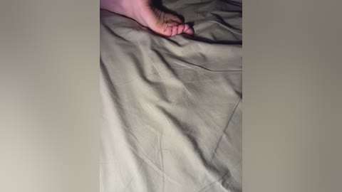A video of a barefoot person lying on a gray bedsheet. The foot, with visible pink toenails, is positioned slightly off-center to the right. The texture of the sheet appears smooth, and the lighting is soft, casting minimal shadows.