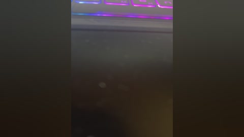A blurry video showing a laptop keyboard with colorful LED lights, partially covered by a dark, possibly furry object, creating a mysterious and slightly eerie atmosphere.