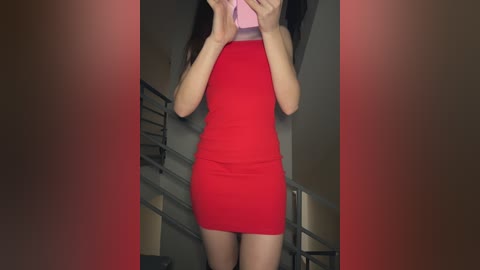 Media: Video of a slender East Asian woman with long dark hair wearing a tight, sleeveless red dress, standing on a modern staircase with metal railings in a dimly lit room.