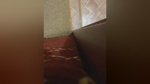 A video showing a corner of a room with a textured, light brown wall, a polished, red-brown wooden floor, and a beige, tiled wall with a diamond pattern. The angle is from the floor looking up.