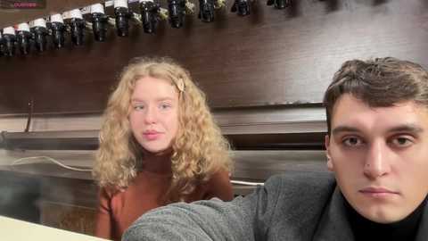 Media: A video of a young man with short dark hair in a gray jacket, sitting next to a young woman with curly blonde hair, both looking serious.