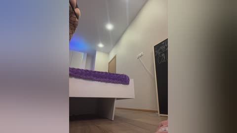 Media: Video of a modern, minimalistic bedroom with white walls, a white bed covered in a purple blanket, and a chalkboard with \"I love you\" written on it.