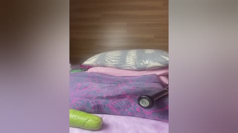 Video of a messy bed with a purple quilt, pink pillow, green cucumber, and a black vibrator, set against a wooden headboard.