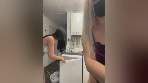 Media: A video of a woman with long black hair, wearing a black bra, scrubbing a white dishwasher in a modern kitchen with black countertops and white cabinets.