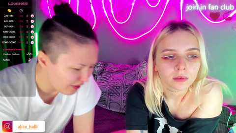 Video of two women, one with short hair, the other with long blonde hair, sitting on a couch under neon lights.