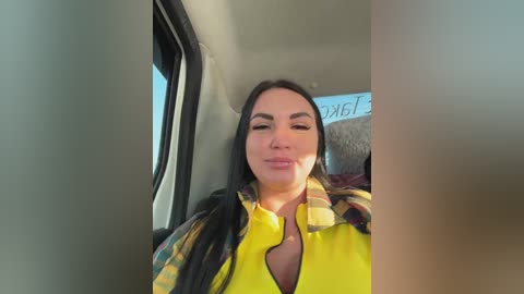 Video of a Latina woman with long black hair, wearing a yellow shirt, sitting in a car, looking out the window.