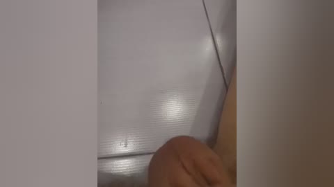 Video of a person's hand with a light skin tone, partially visible, holding a shiny, reflective object (possibly a mirror or a piece of glass), against a white background.
