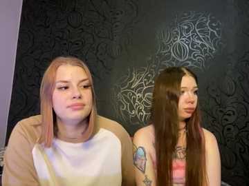 Media: Video of two young women with long, straight hair, one in a beige top, the other in a pink tank top. Dark, ornate wallpaper background.