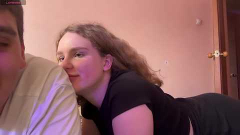Media: A video showing a fair-skinned woman with curly brown hair, wearing a black top, leaning over a white-shirted man, kissing him passionately in a dimly lit room.