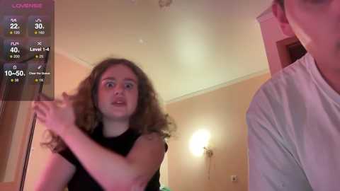 Media: A video of a young woman with curly hair, wearing a black top, standing in a dimly lit room, seen from a live stream angle, with a weather display in the top left corner.