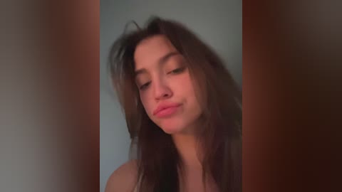 A blurry video of a young woman with long, dark hair, wearing a black tank top, against a plain, neutral background. She has a neutral expression, with slightly parted lips.
