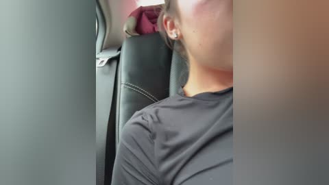 Media: Video of a person with light skin, wearing a black shirt, seated in a car. The image is slightly blurred, showing the side profile of the person.