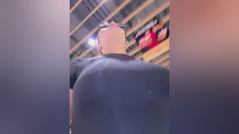 Media: Video of a bald, middle-aged man in a black shirt, standing with his back to the camera, facing a large, blurred television screen displaying a football game.