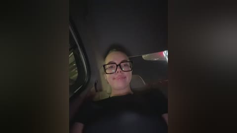 Media: A video of a woman with glasses and a dark top, smiling while driving at night. The interior of the car is dimly lit, and the view is partially obstructed by a rear-view mirror.