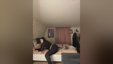 Media: Video of a young woman with dark hair and fair skin, wearing black clothing, lying on a bed in a dimly lit bedroom with beige walls, a pink curtain, and a Star Wars poster.