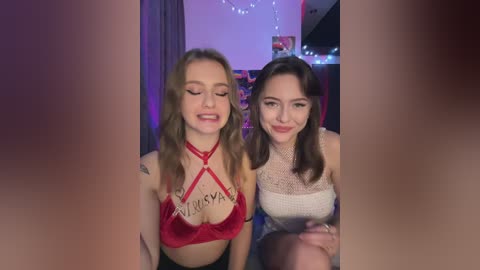 Media: Video of two young women in lingerie, one with a red halter top, the other in a white lace top, seated in a dimly lit room with fairy lights.