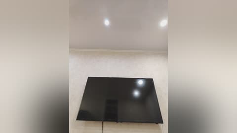 Video of a minimalist living room with a large, sleek black flat-screen TV mounted on a light beige wall. The room features soft, warm lighting and clean lines, creating a modern, uncluttered aesthetic.