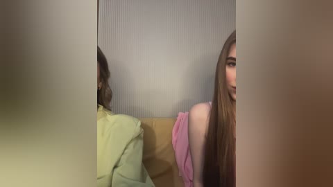 Media: Video of a woman with long, straight brown hair, wearing a pink shirt, sitting on a beige couch with a yellow pillow behind her, reflected in a mirror, creating a distorted, surreal effect.
