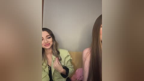 Media: Video of two women in a dimly lit room. One woman with long, wavy hair and a light green jacket playfully pulls the other's long, straight hair. The background shows a wooden door and a textured wall.