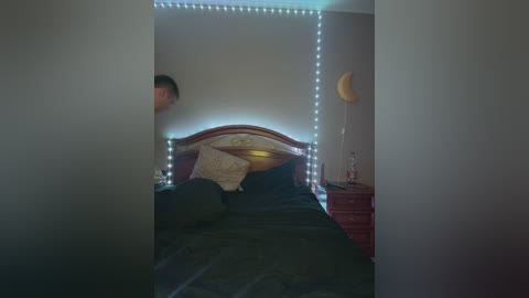 Media: Video of a dimly-lit bedroom with a man in motion, a bed with a wooden headboard, a crescent moon wall decal, and a string of white lights.