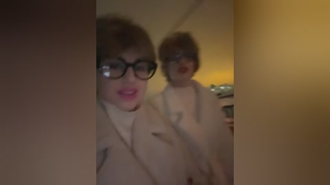 Media: A video of a woman with short, curly hair and glasses, wearing a beige coat, standing in front of a mirror. The background is dimly lit, creating a slightly blurred, vintage ambiance.