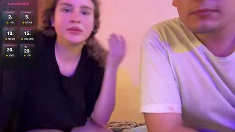 Media: Video of a young woman with curly hair and a man in a white t-shirt, both seated indoors, with a purple-pink lighting.