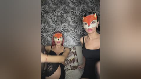 Video of two women in black lace lingerie, one with red hair and a fox mask, the other with dark hair and a cat mask, against leopard-print wallpaper.