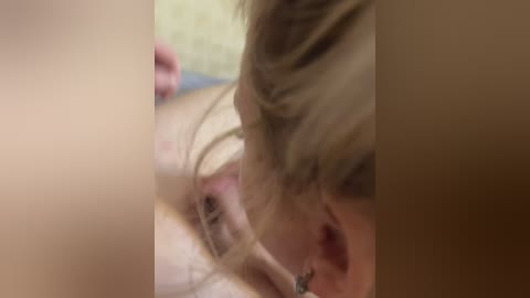 Video of a close-up of a person with light blonde hair, fair skin, and glasses, focusing on their face, partially obscured by a fuzzy, blurred figure.