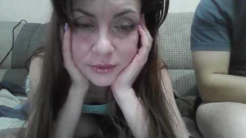 Video of a young Caucasian woman with long brown hair, lying on a couch, resting her head on her hands, looking tired and contemplative.
