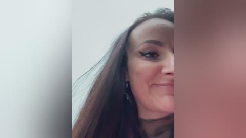 Media: Video of a smiling woman with long brown hair, wearing black eyeliner and earrings, partially obscured by a vertical, blurred object.