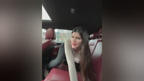 Media: A video of a smiling woman with long brown hair, wearing a light-colored top, seated in a red leather car seat with black accents. The car's interior is visible, with a sunroof letting in light.