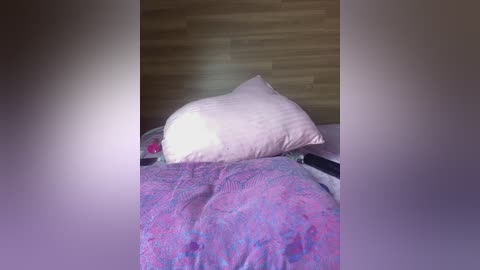 A video of a bed with a white pillow on a purple and blue floral-patterned comforter. The headboard is wooden, and the lighting is soft, creating a cozy, intimate atmosphere.