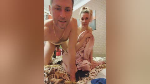 Media: A video shows a topless man with a short beard and a muscular build, and a blonde woman with large breasts, both on a leopard-print bed in a dimly lit room.