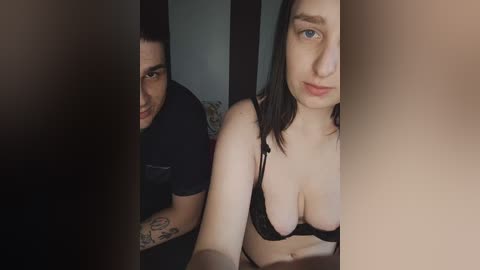 Video: A woman with medium-length dark hair, wearing a black bra, sits in front of a man with short dark hair, both in dimly lit room.