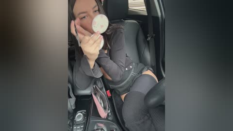 Media: A video shows a young woman with medium brown skin and shoulder-length dark hair, wearing a black top, denim shorts, and thigh-high socks. She is seated in a car, holding a phone to her ear.