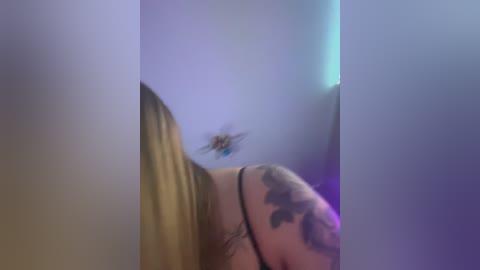 Media: Video of a close-up view of a tattooed arm, blurred and indistinct, with a light blue, purple, and white color gradient in the background.