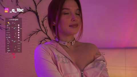 A young woman with light skin and long brown hair, wearing a white jacket with a heart-shaped zipper pull, stands in a dimly lit room with pink and purple hues.